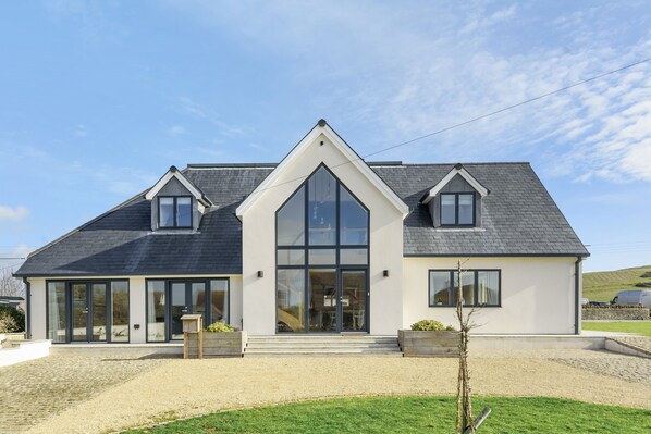 A modern two-story house with large glass windows, a steeply pitched roof, and a gravel driveway.
