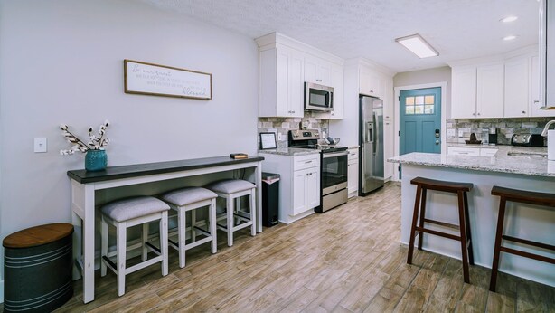 A modern kitchen with white cabinets, a central island with stools, a microwave, oven, and refrigerator. - Homestead @ Oakley Farms (Cumming)