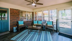 A sunroom with a brick wall, large windows, a ceiling fan, and a seating area with cushions. - Homestead @ Oakley Farms (Cumming)