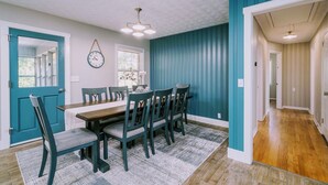 A dining area with a wooden table and chairs, a clock on the wall, and a blue accent wall. - Homestead @ Oakley Farms (Cumming)