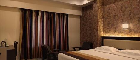 A hotel room with a bed, a desk, a chair, and a ceiling fan.