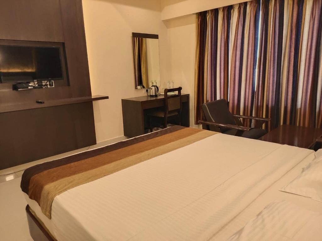 Quarto de hotel com uma cama grande, uma mesa com cadeira, televisão e janela com cortinas.
