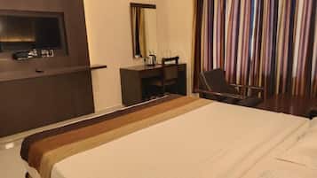 Quarto de hotel com uma cama grande, uma mesa com cadeira, televisão e janela com cortinas.