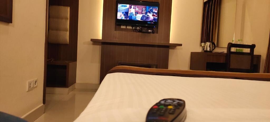 A hotel room with a bed, a television mounted on a wall, and a remote control on the bed.