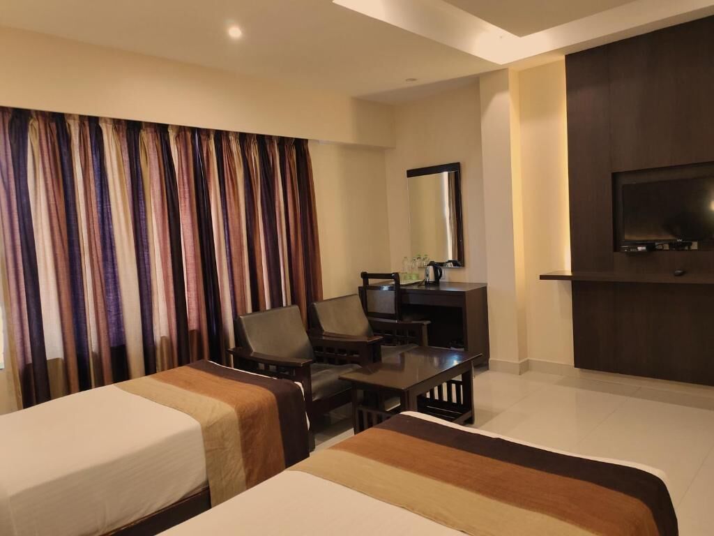 A hotel room with two beds, a desk, a chair, a television, and a large mirror.