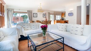A spacious living room with white sofas, a glass coffee table, and a view of the outside. - Villa Goshen - Praia da Luz (Luz)