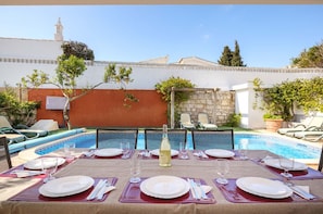 An outdoor dining area with a pool, tables set for four, and lounge chairs. - Villa Goshen - Praia da Luz (Luz)