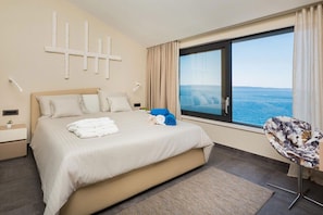 Une chambre d’hôtel avec un grand lit, une vue sur la mer, une chaise et une table de chevet.