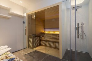 A modern bathroom with a glass-enclosed sauna, a wooden bench, and a shower area.
