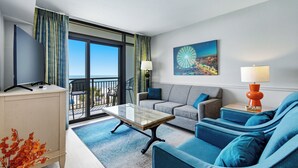 Habitació d'hotel amb balcó, sofà, taula de cafè, televisió i làmpada.
