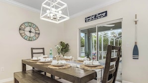 A dining area with a wooden table set for four, a clock, and a sign reading "Coastal Living". - Family Oasis: Waterfront Heated Pool & Game Room (Cape Coral)