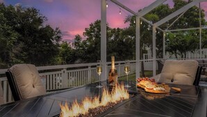 An outdoor patio with a glass table, chairs, a fire feature, and a bottle of wine. - Family Oasis: Waterfront Heated Pool & Game Room (Cape Coral)