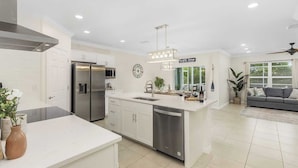 A modern kitchen with white cabinetry, stainless steel appliances, and a central island. - Family Oasis: Waterfront Heated Pool & Game Room (Cape Coral)