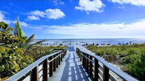 A wooden boardwalk leading to a beach with people and palm trees. - Family Oasis: Waterfront Heated Pool & Game Room (Cape Coral)