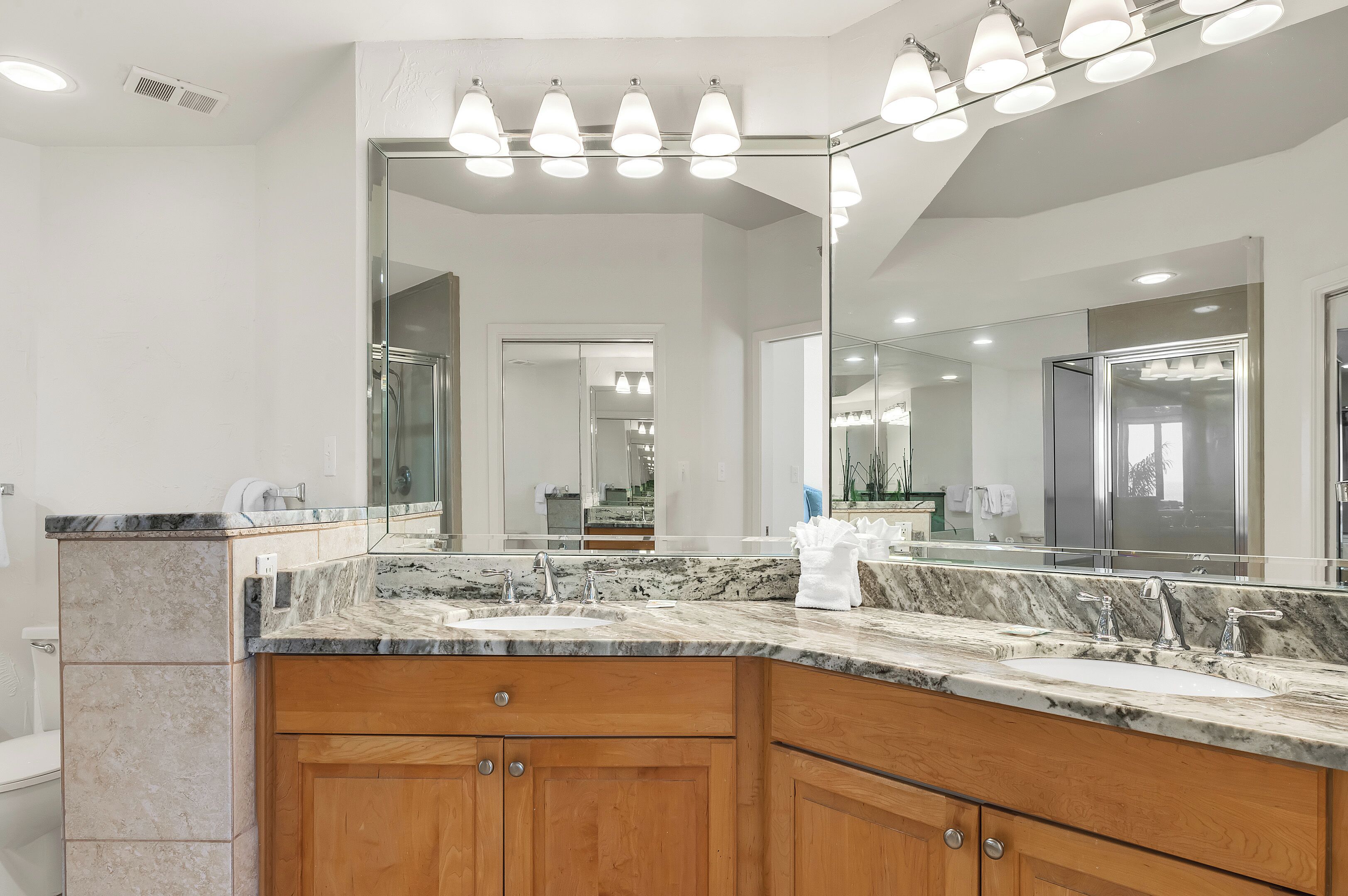 A bathroom with a large mirror, a marble countertop, and wooden cabinets.