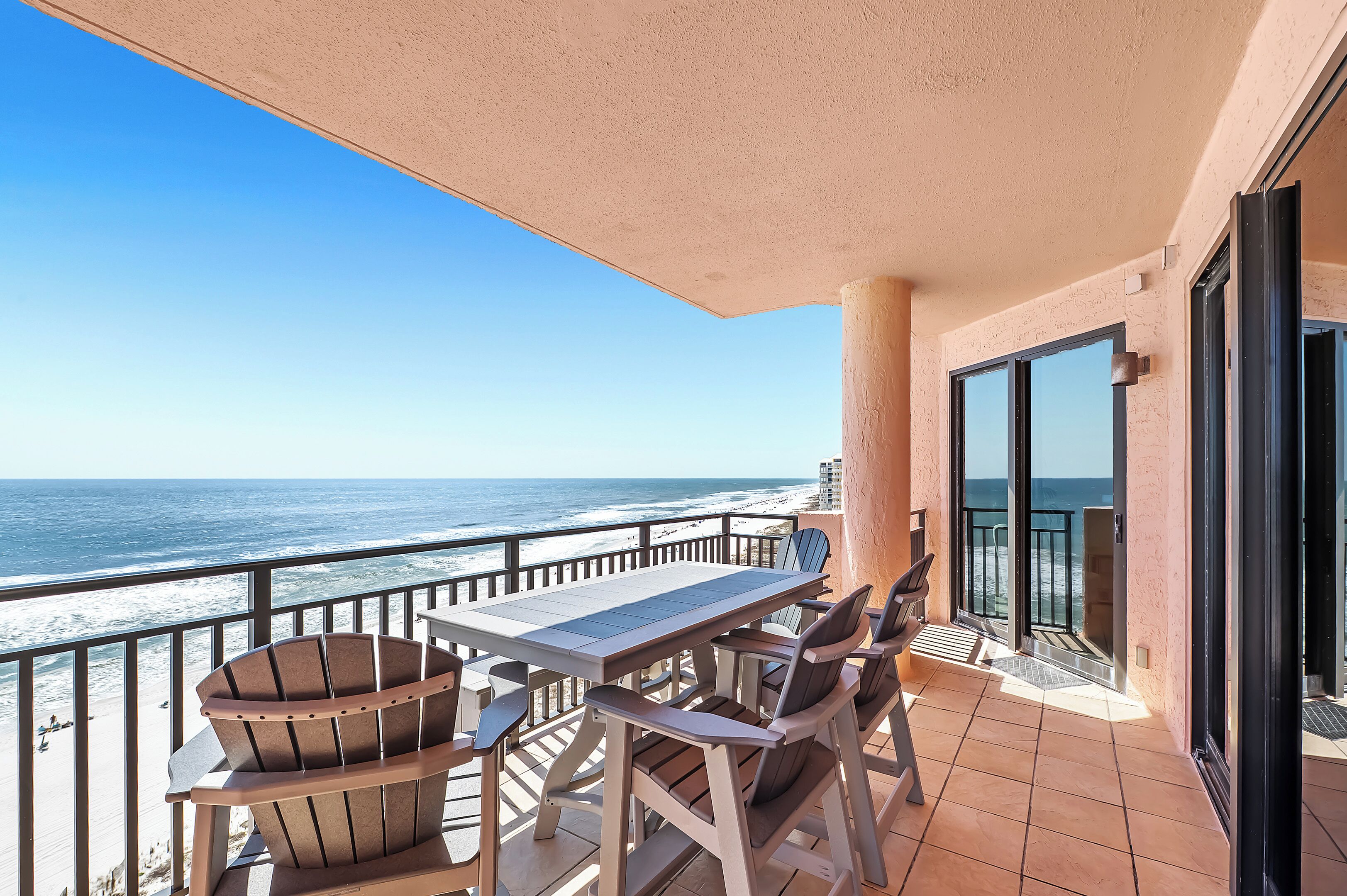 Un balcon avec une table et des chaises, donnant sur une plage et l’océan.