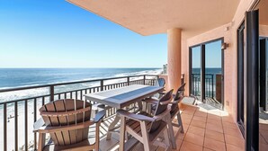 Un balcon avec une table et des chaises, donnant sur une plage et l’océan.