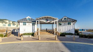 A beachfront building with a covered entrance, a clock, and a view of the ocean. - Sound front home w boat slip! New for 2026 pool! (Wrightsville Beach)