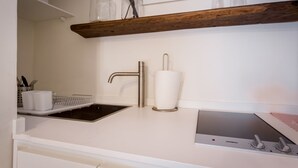 Una cocina con un lavamanos de acero inoxidable, una estufa empotrada y un estante de madera sobre el lavamanos.