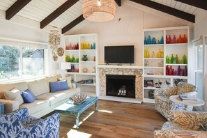 Ein Wohnzimmer mit Kamin, Fernseher und farbigen Glasflaschen in Regalen.