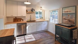 Una cucina con mobili bianchi, una lavastoviglie in acciaio inossidabile, un piano di lavoro in legno, un armadietto verde e un quadro a tema spiaggia.