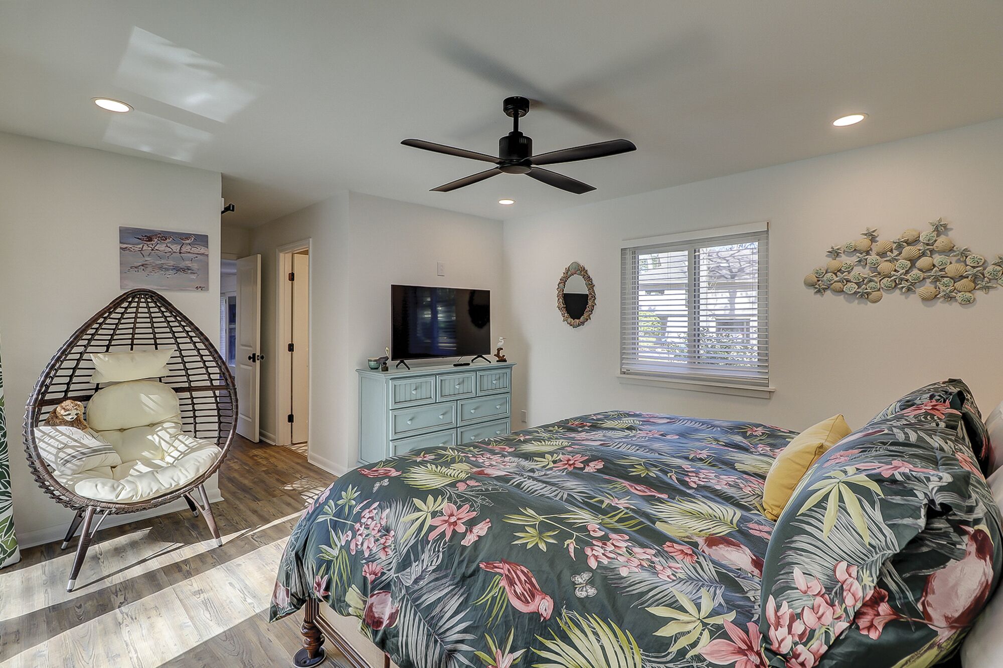 A bedroom with a bed, a ceiling fan, a television, a dresser, and a chair.