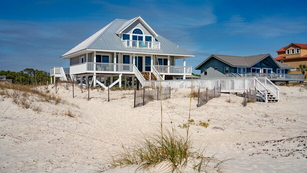 Une maison située en bord de mer, dotée d’un grand balcon, d’une véranda et d’un escalier menant à l’entrée principale.
