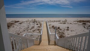 Un escalier en bois menant à une plage, avec un ciel dégagé.