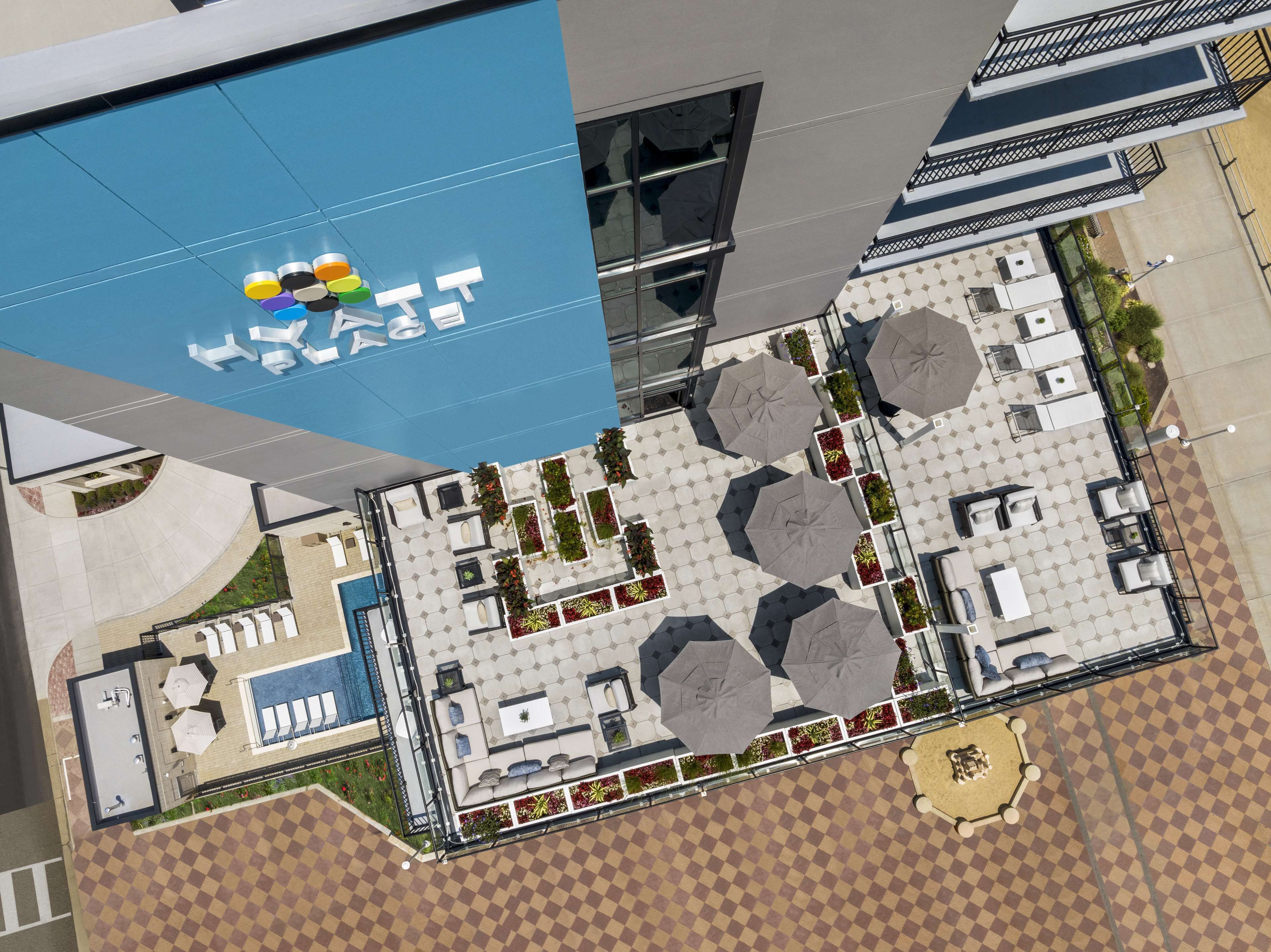 An aerial view of a hotel with a pool, outdoor seating, and a blue awning with a logo.