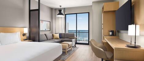 Ein modernes Hotelzimmer mit einem großen Bett, einem Schreibtisch, einem Stuhl, einer Couch, einem Fernseher und einem Balkon mit Aussicht.