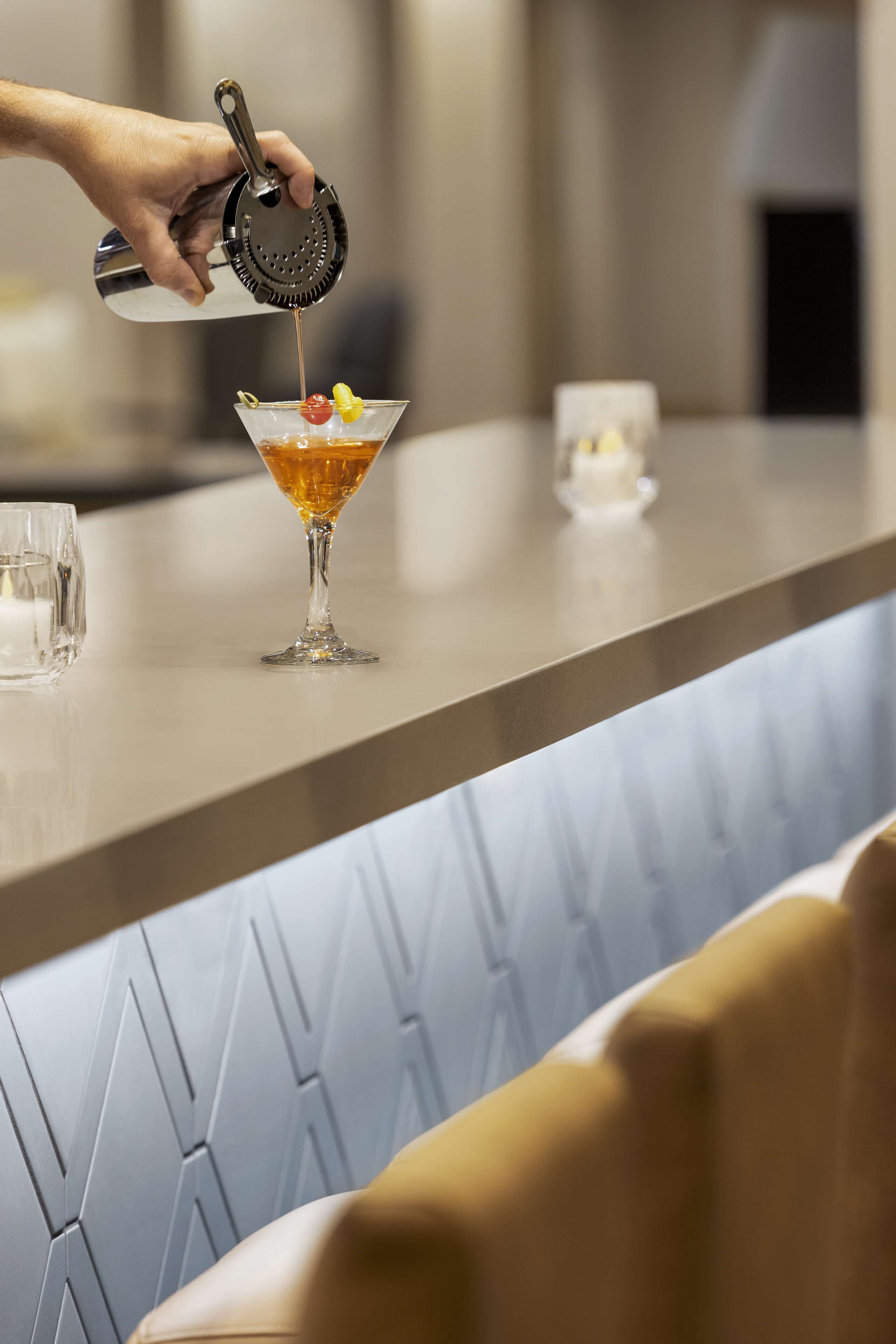 A bar setting with a martini glass on a counter, a cocktail shaker, and a small glass.