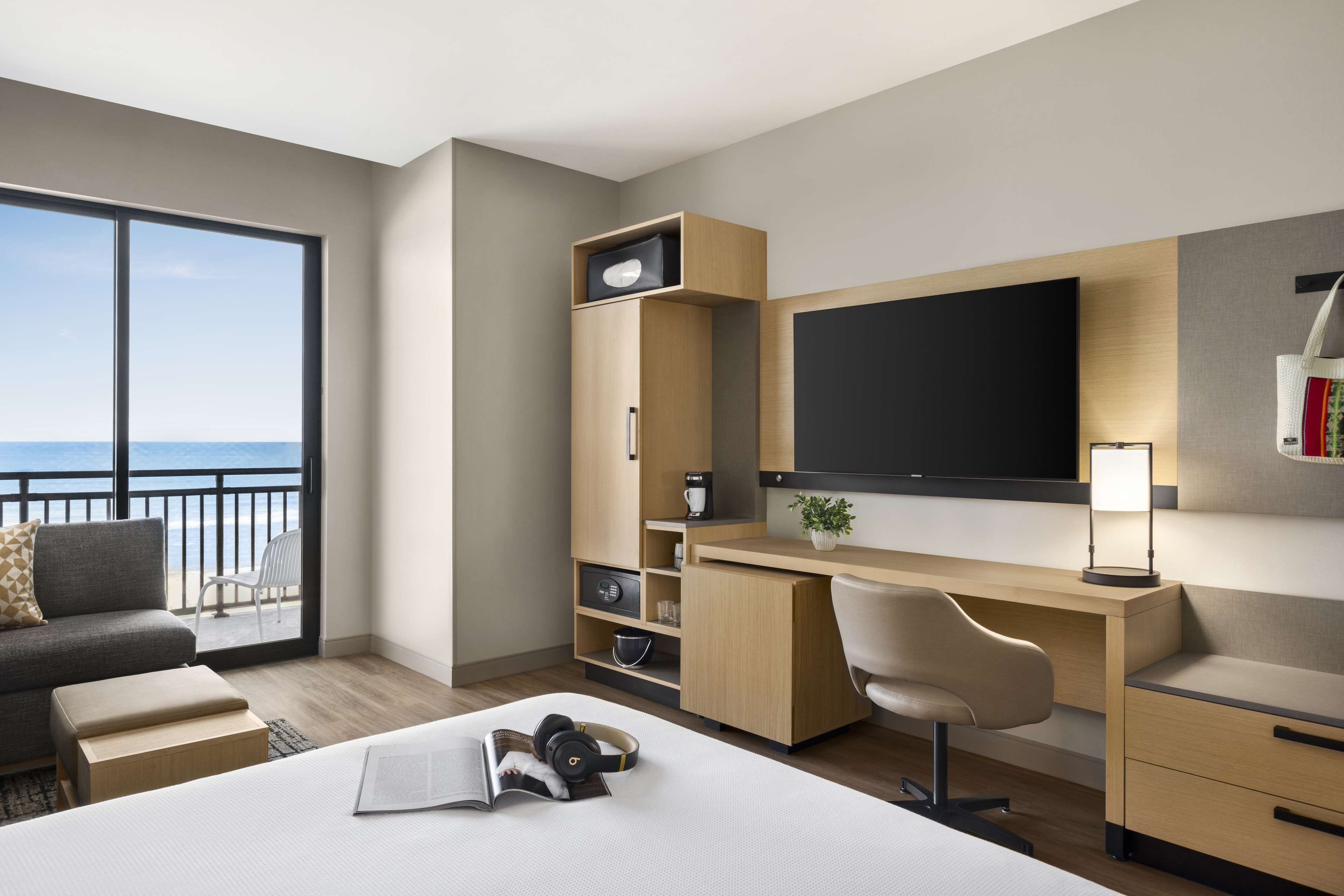 Una habitación de hotel moderna con una cama grande, un escritorio con televisor de pantalla plana, un sofá y un balcón con vista al mar.