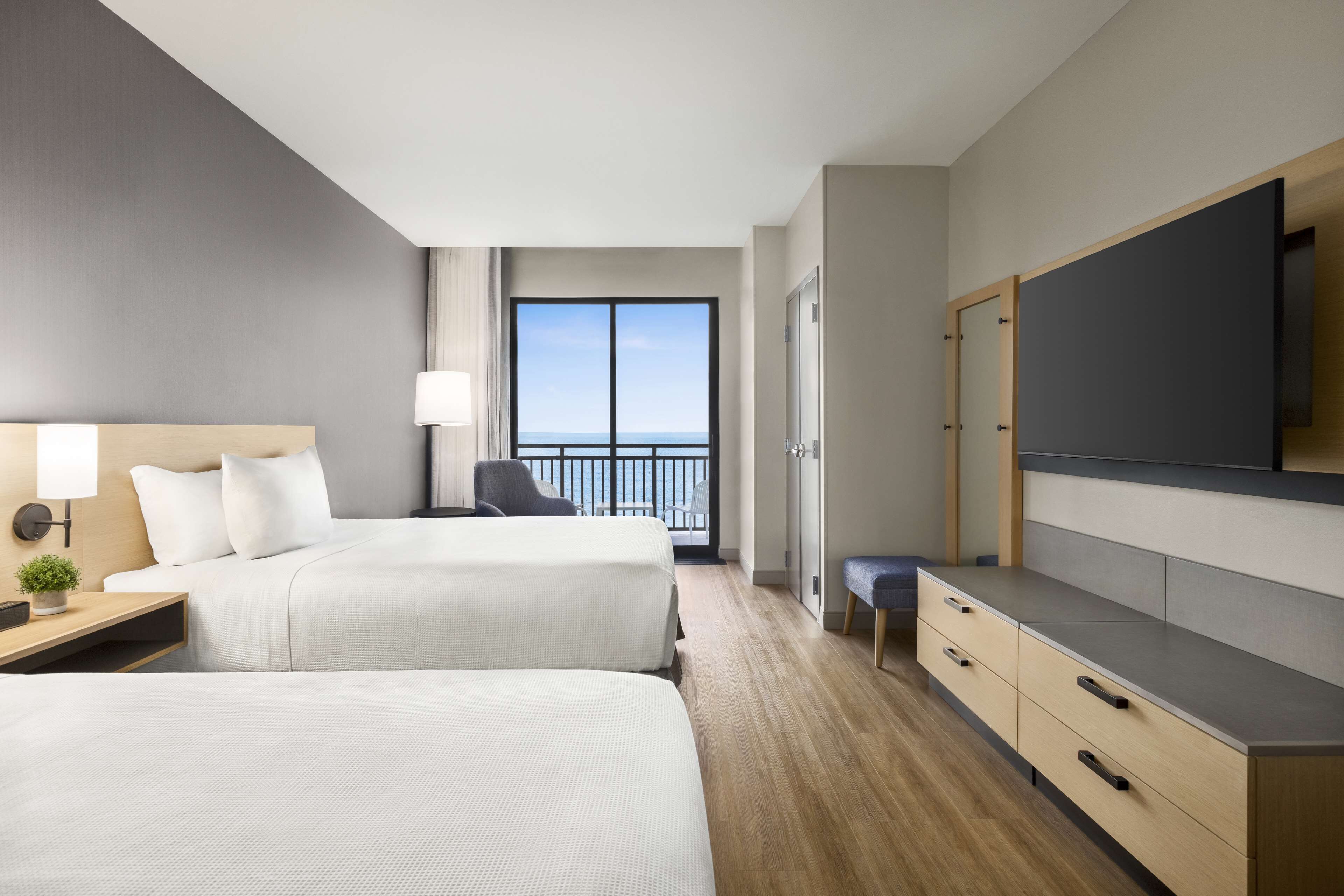 Une chambre d’hôtel avec deux lits, une télévision, un bureau avec une lampe et une vue sur la mer.