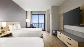 Une chambre d’hôtel avec deux lits, une télévision, un bureau avec une lampe et une vue sur la mer.