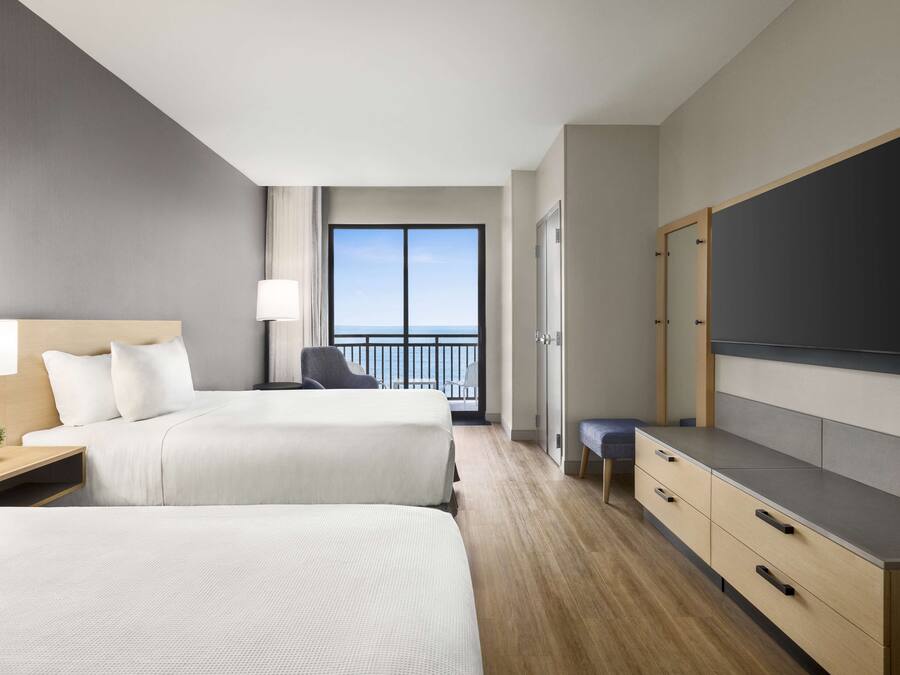 Une chambre d’hôtel avec deux lits, une télévision, un bureau avec une lampe et une vue sur la mer.