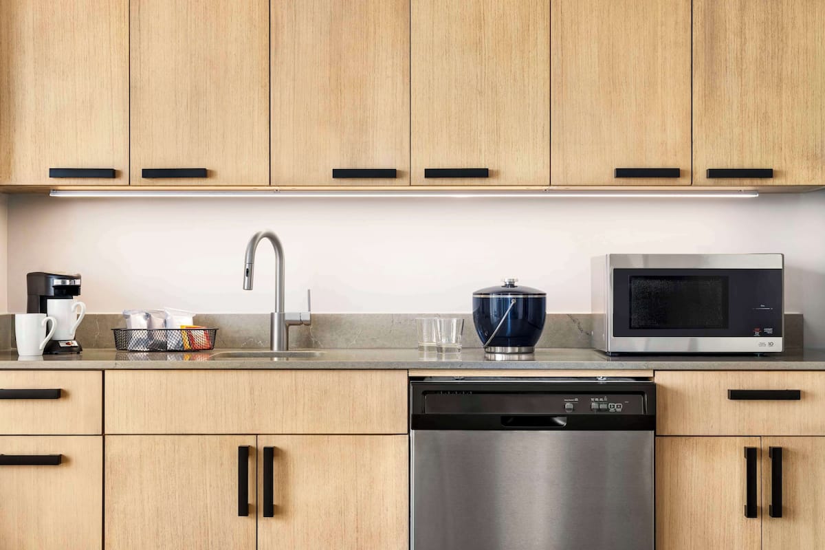 A modern kitchen with wooden cabinets, a stainless steel dishwasher, a microwave, and a coffee maker.