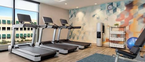 A gym with treadmills, a bench, dumbbells, and a wall clock.