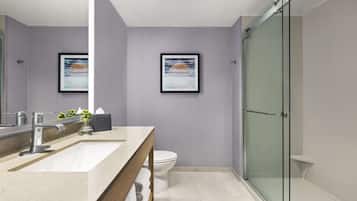 A modern bathroom with a large mirror, a glass shower enclosure, and two framed artworks on the wall.