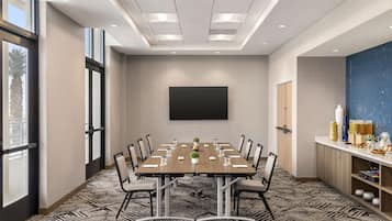 A conference room with a large table, chairs, a projector screen, and a kitchenette area.