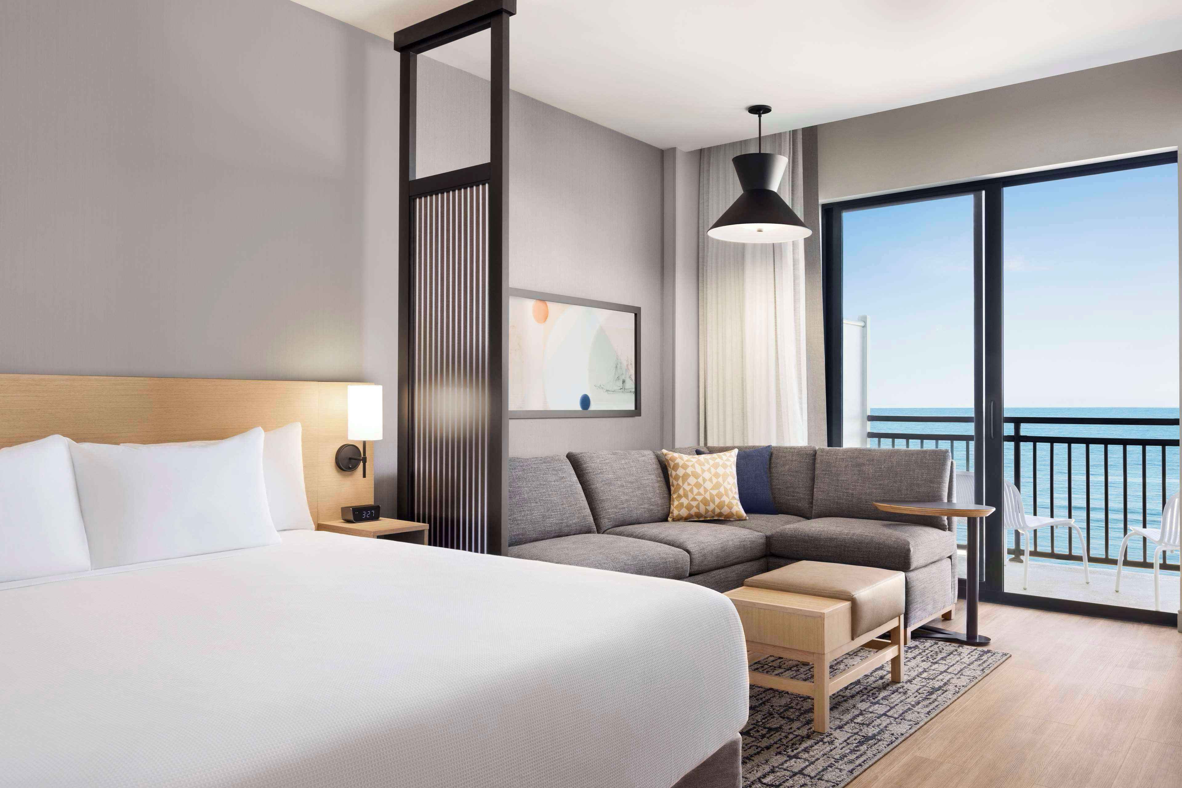 Een moderne hotelkamer met een groot bed, een bank, een klein tafeltje en een balkon met uitzicht op zee.