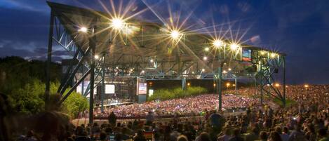 A large outdoor amphitheater with tiered seating and a stage, surrounded by a crowd of people.