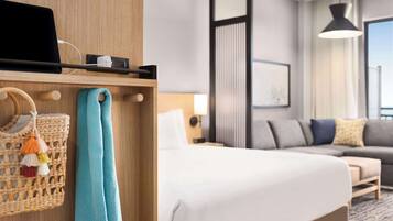 A hotel room with a bed, a sofa, a desk with a laptop, a lamp, and a large window.