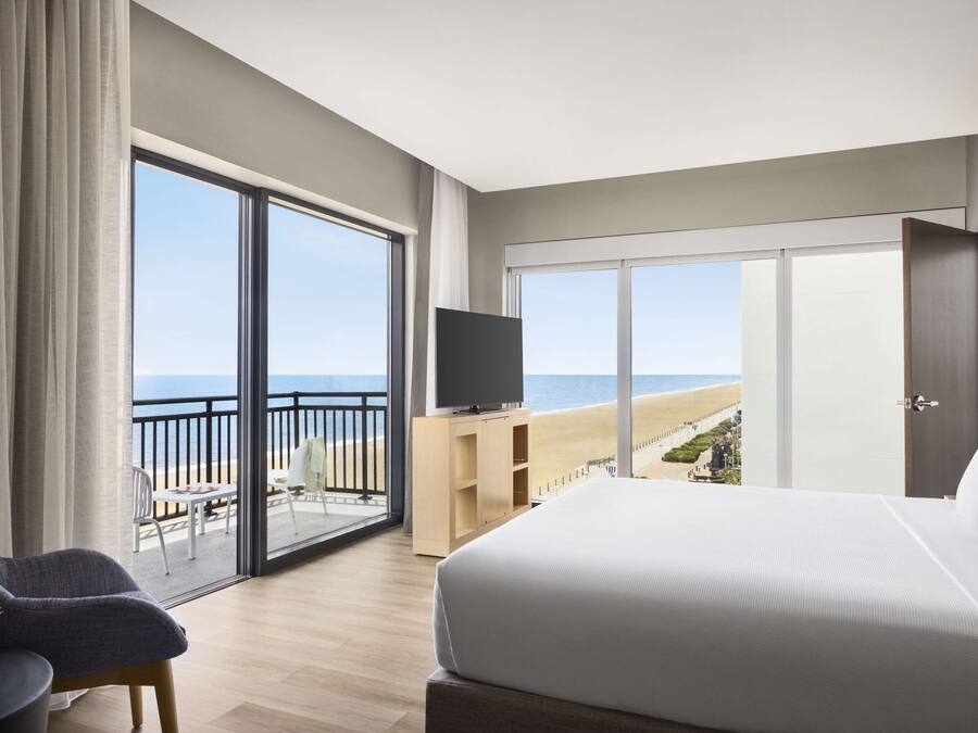Une chambre d’hôtel dotée d’un grand lit, d’une télévision, d’un balcon avec vue sur la plage et d’un coin repas.