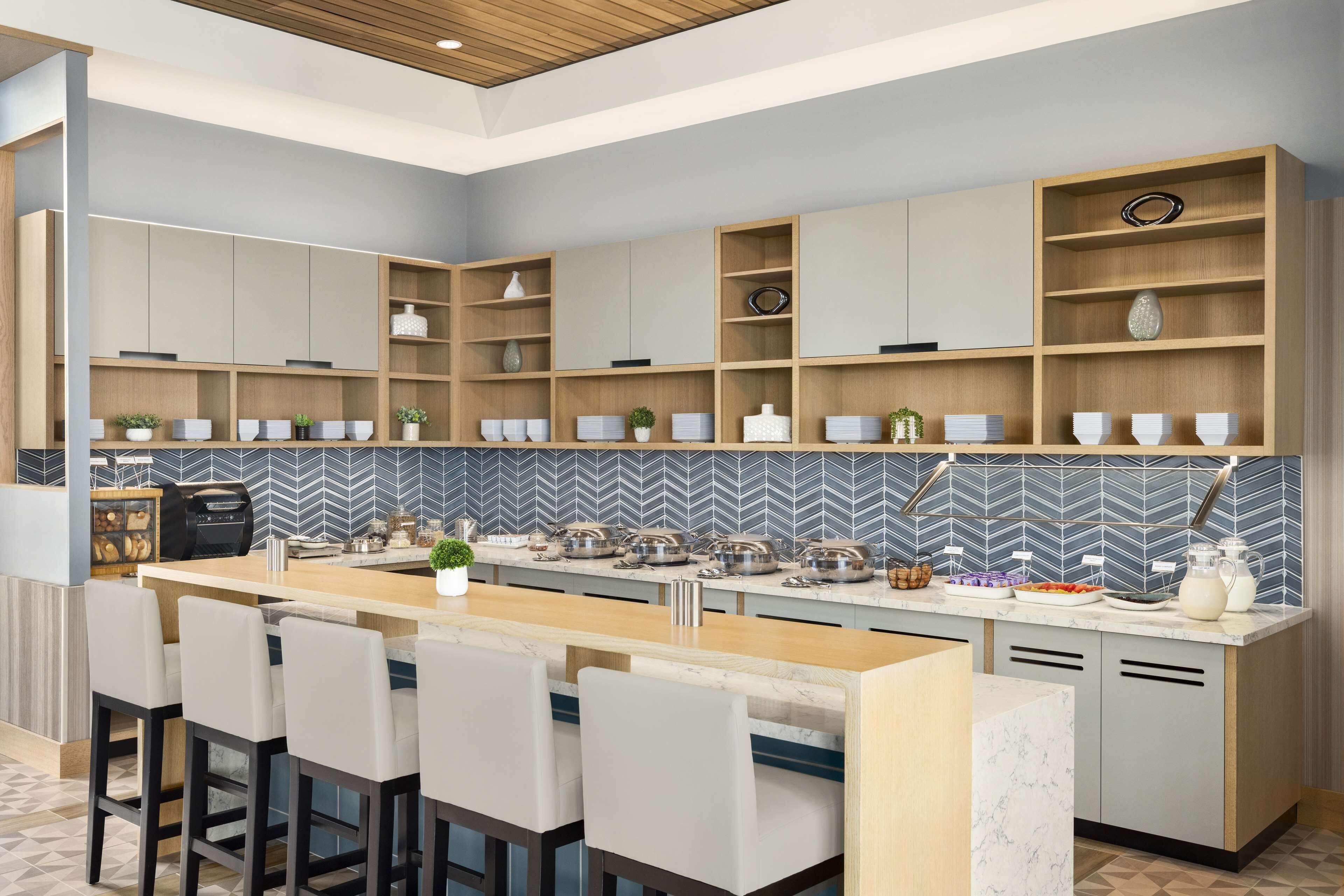 Een moderne keuken met inbouwmeubels, een centraal kookeiland met barstoelen, en een backsplash van visgraatmozaïek.