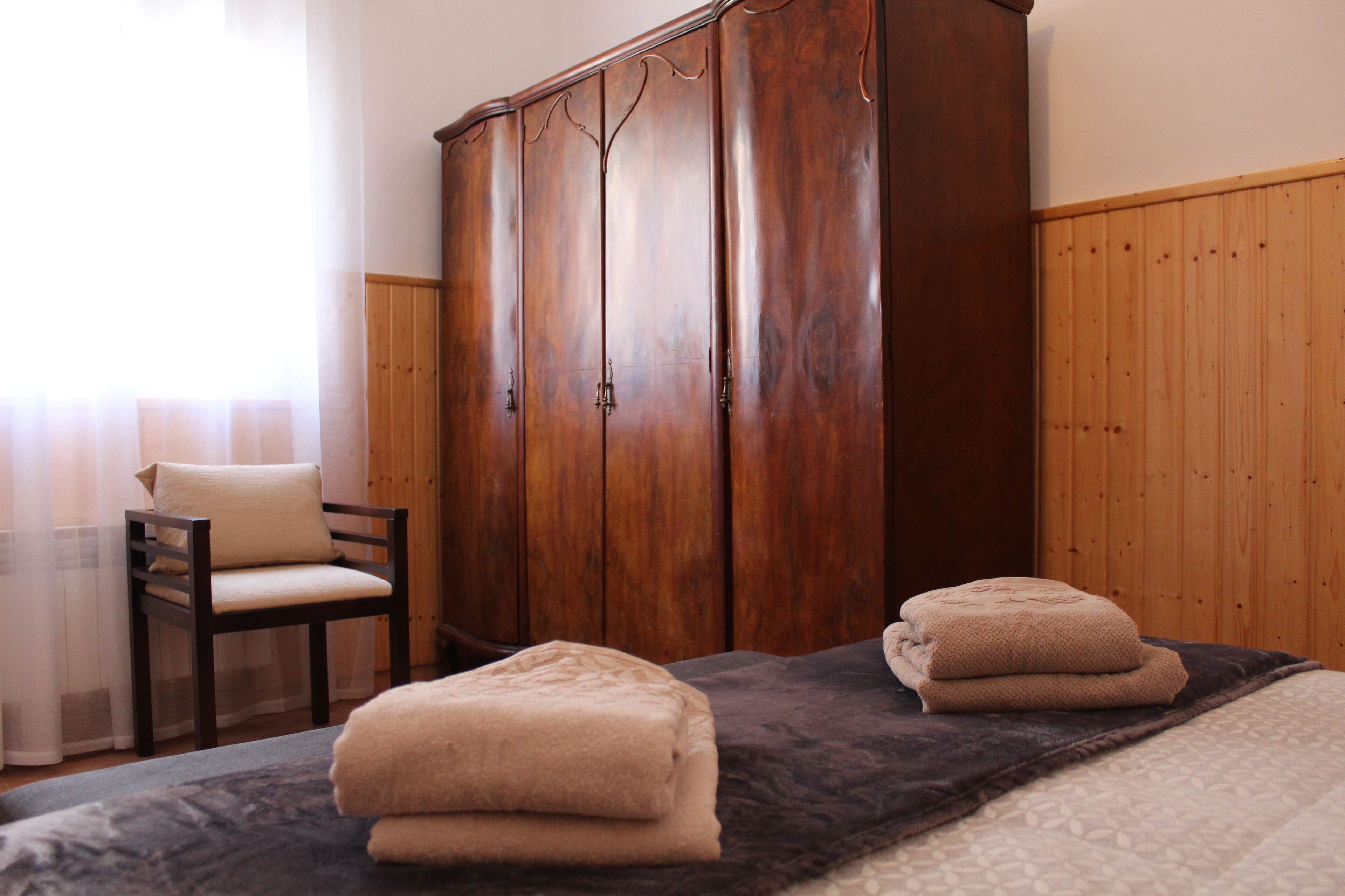 Une pièce comprenant un lit, une armoire en bois, une chaise et une fenêtre avec des rideaux.