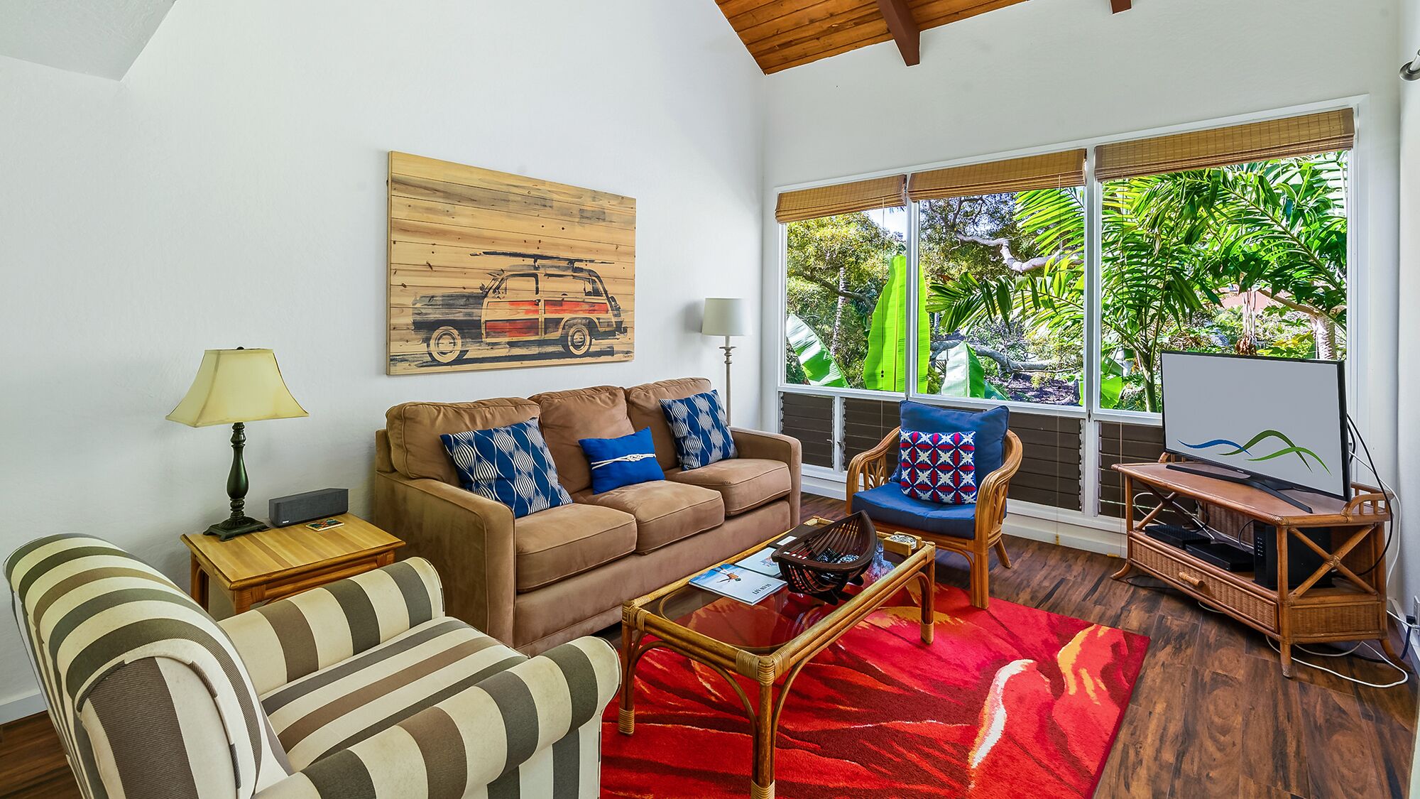 A living room with a sofa, armchair, and a red rug. There is a painting on the wall and a TV on a stand.