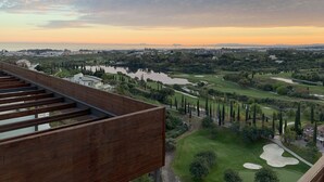 Une vue panoramique d’un terrain de golf, avec une rivière, des arbres et des bâtiments en arrière-plan.