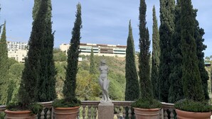 Une fontaine ornée d’une statue au centre, entourée de grands cyprès et de jardinières en terre cuite.
