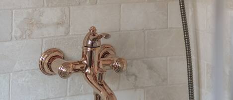 A shower with a handheld showerhead and a wall-mounted faucet.