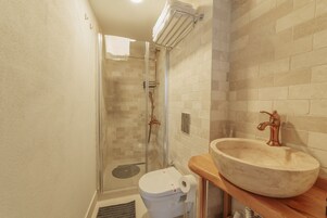 A bathroom with a glass-enclosed shower, a white toilet, and a large vessel sink with a copper faucet.
